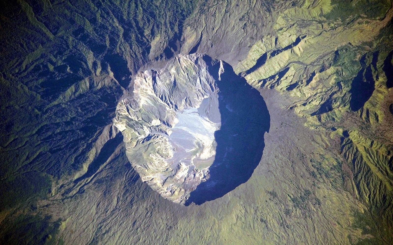 Aerial view of Mount Tambora's massive volcanic crater surrounded by green vegetated slopes
