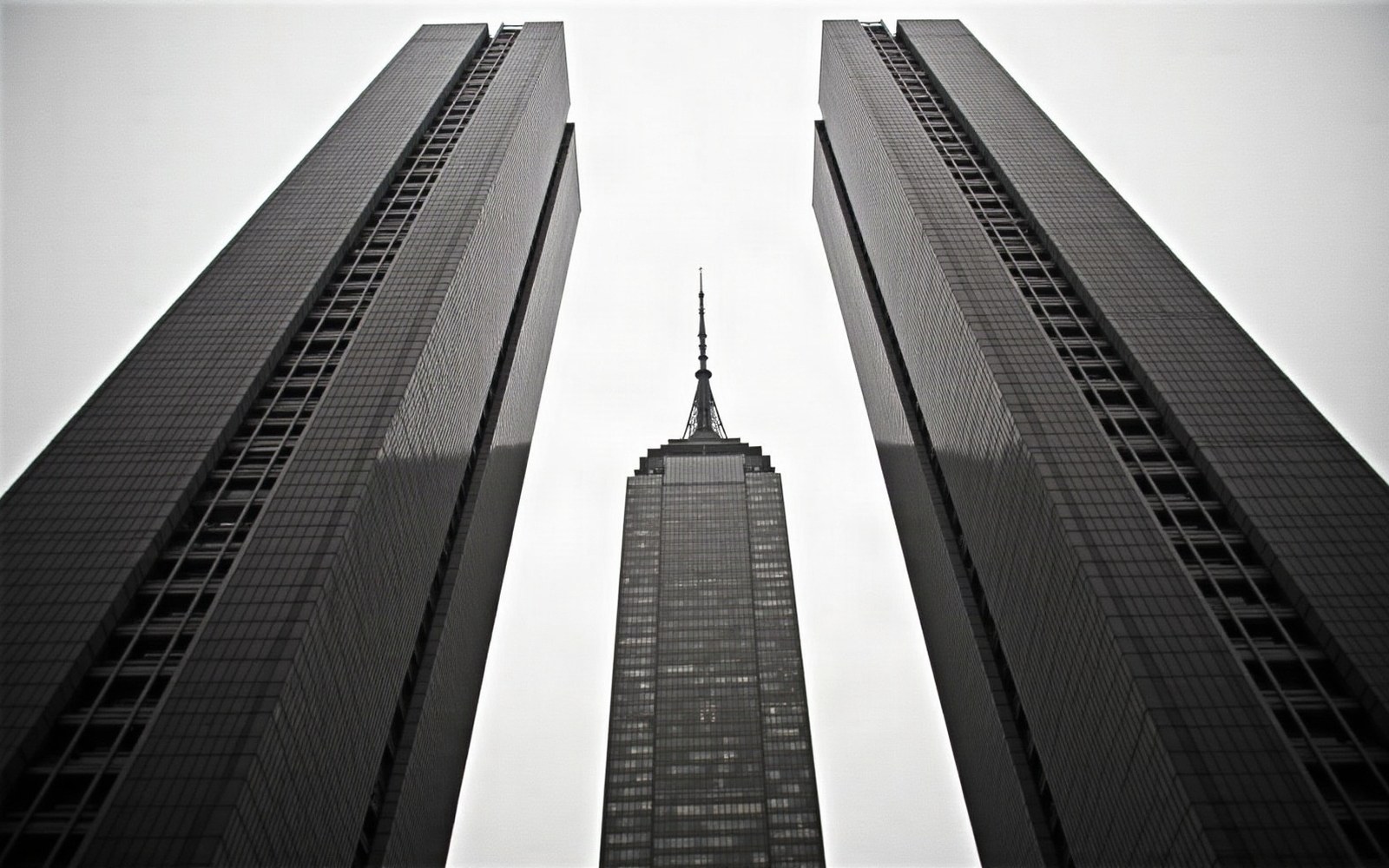A spired skyscraper rises between two flanking towers, viewed from street level