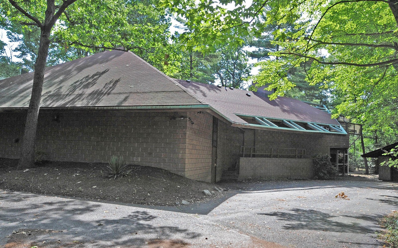 Low brick building with a steep pyramidal roof surrounded by trees