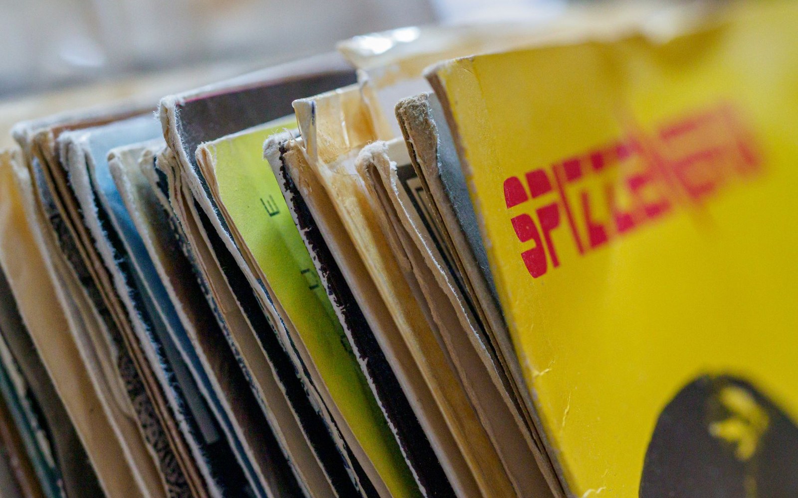 Worn vinyl record sleeves stacked edge-on, showing faded yellow and green cover art